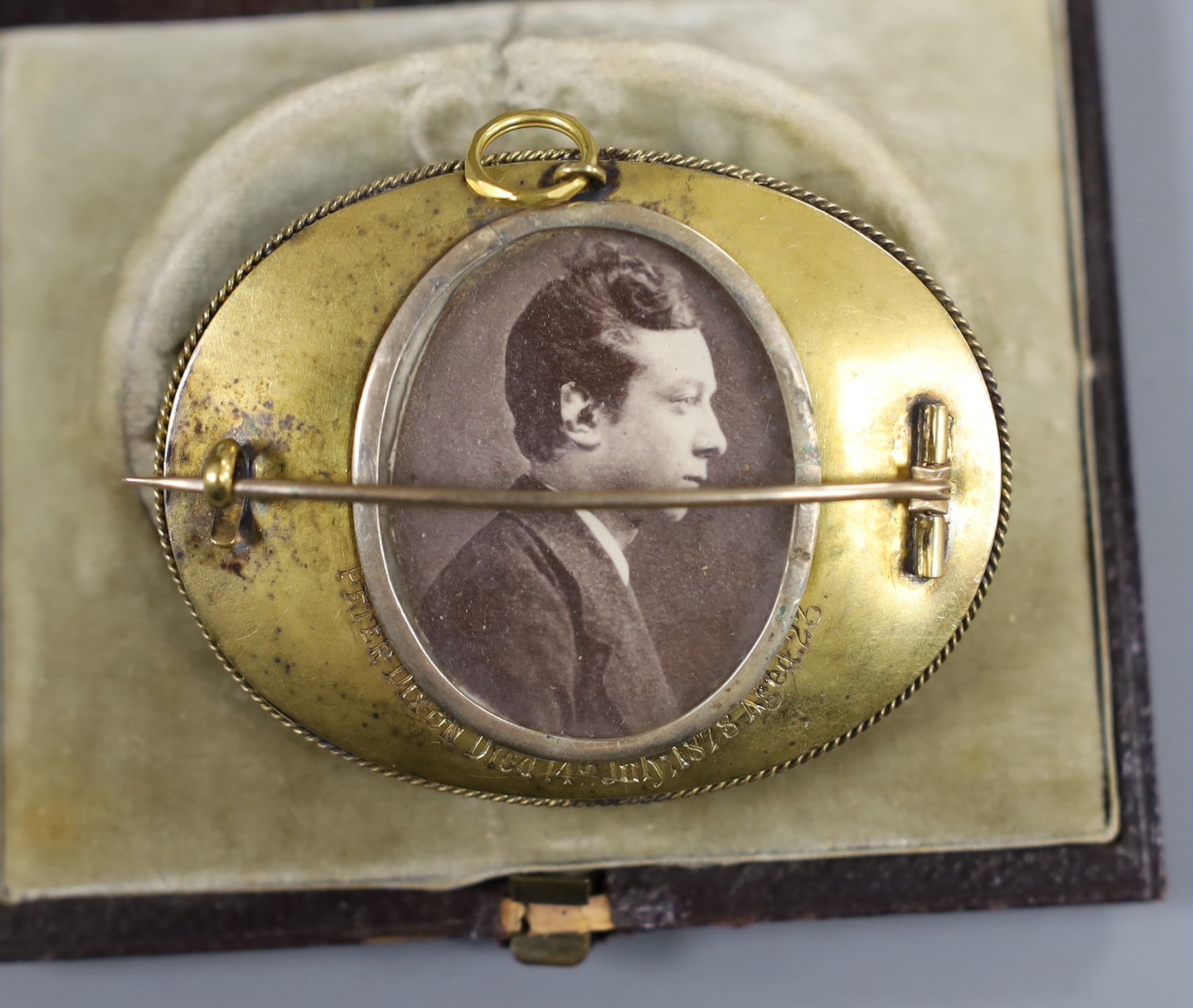 A Victorian yellow metal and black enamel oval memorial brooch, in original box, with plaited hair and inscribed verso 'Peter Dixon Died 14th July 1878 aged 23' with photograph, width 58mm, gross weight 27.9 grams.